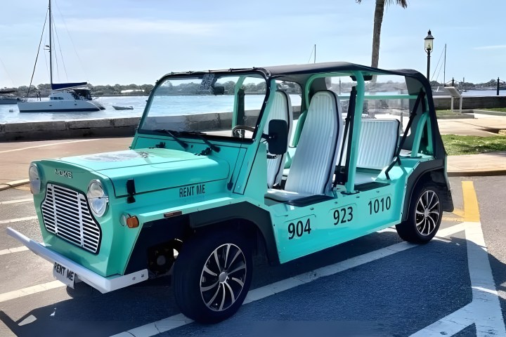 Light blue open-air vehicle parked by a marina with boats and palm trees in view.