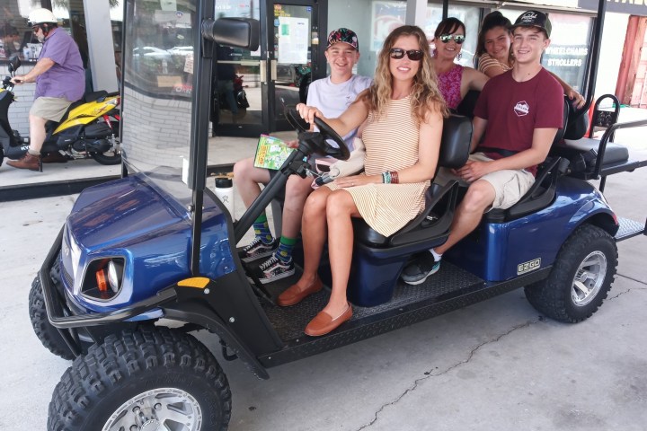 Group of six people smiling while seated in a blue golf cart.