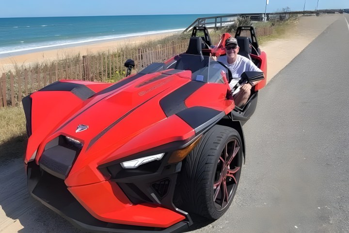 Person in a red three-wheeled vehicle parked by a beach.