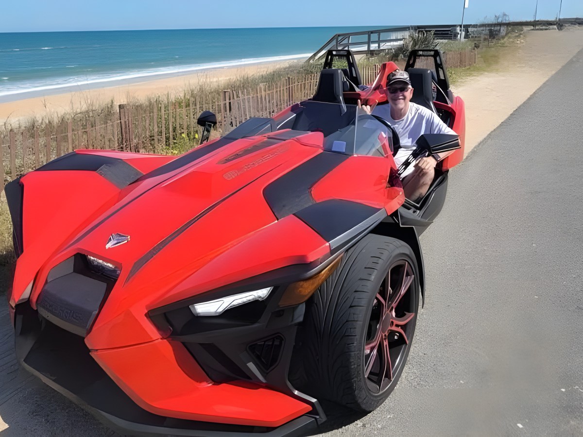 Person in a red three-wheeled vehicle parked by a beach.