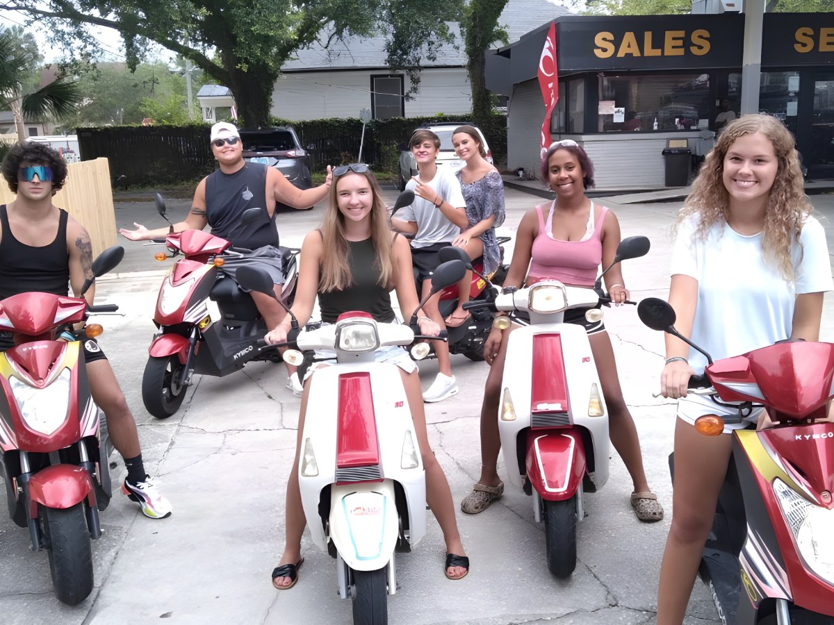 Group of six people on red scooters in parking lot, smiling.