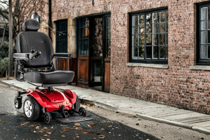 Red mobility scooter parked on a street near a brick building.