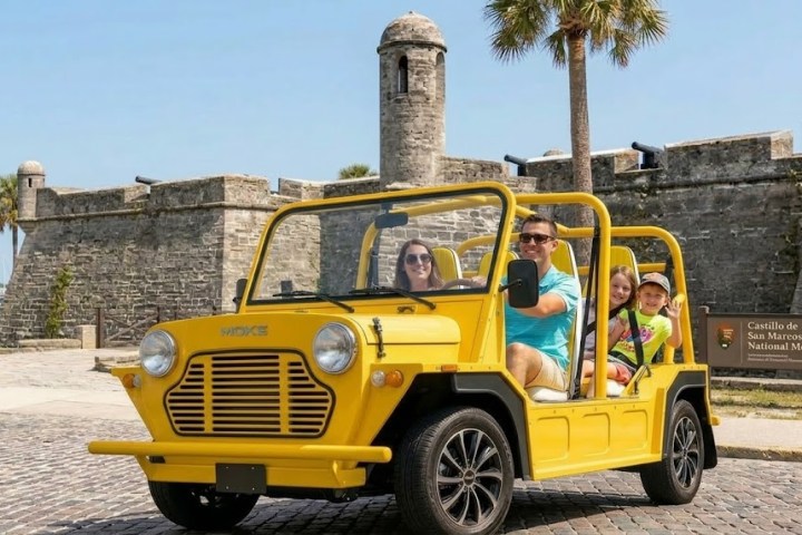 Family in yellow open-top car near historic stone fort with palm trees.