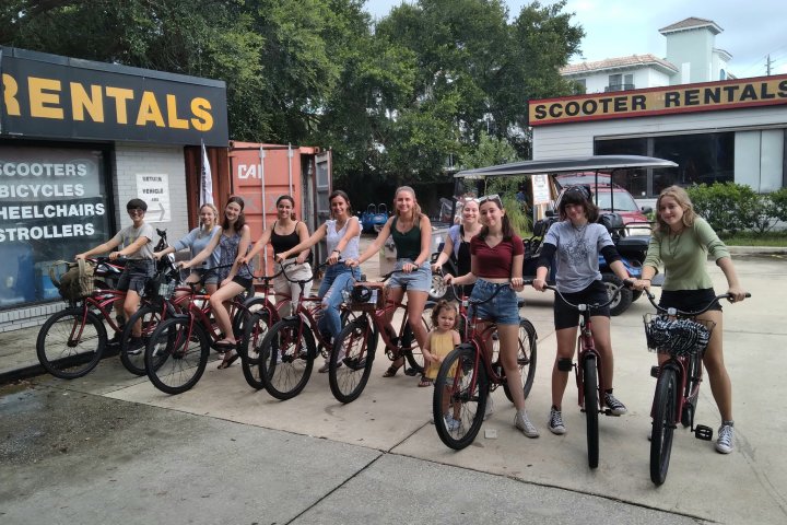 Group of people with bikes in front of a scooter rental shop.