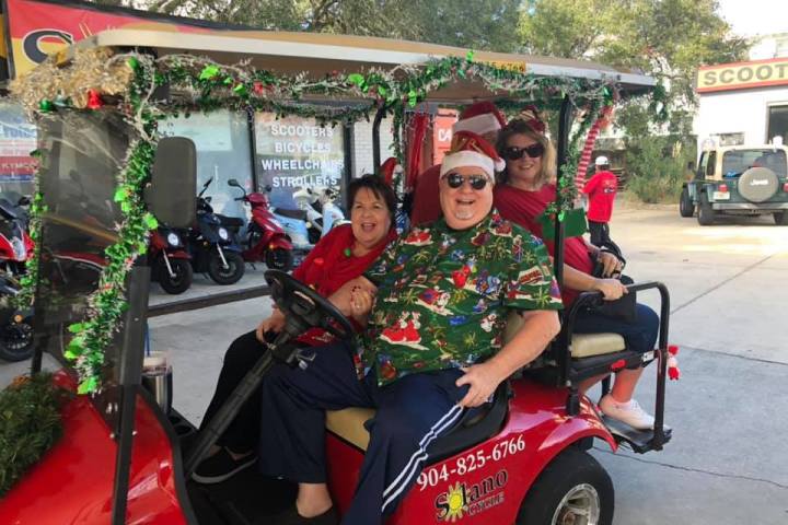 Three people in festive attire riding a decorated red golf cart.