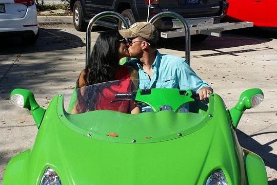 Couple kissing in a small green car at a rental shop.