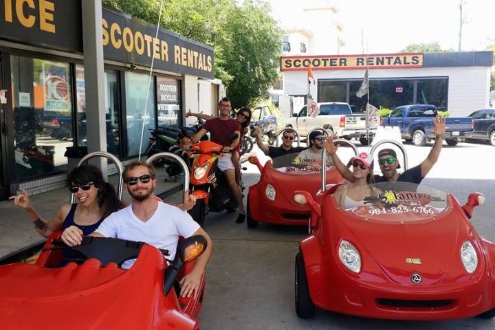 Group of people in red three-wheeled scooters at rental shop.